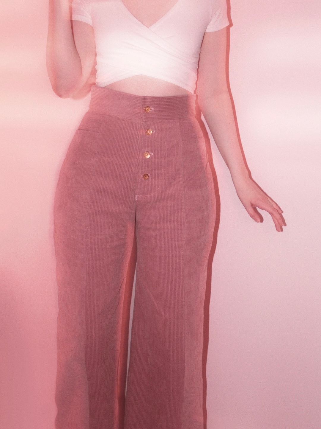 Woman wearing pink corduroy pants with button fly.