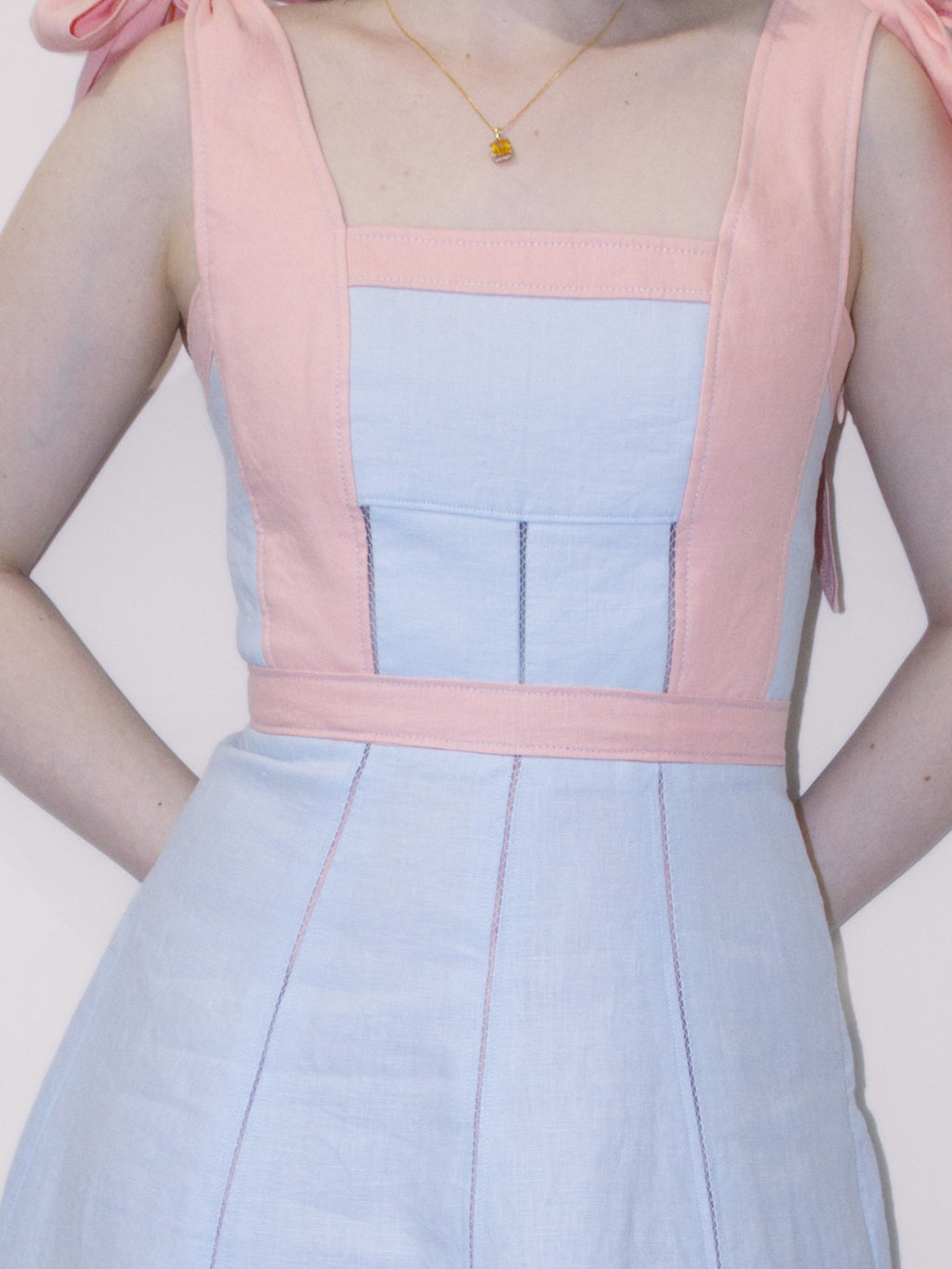 Detail of dress front showing the open stitching in the bodice and skirt. The skirt lining is pink and can be seen through the open stitching in the skirt.