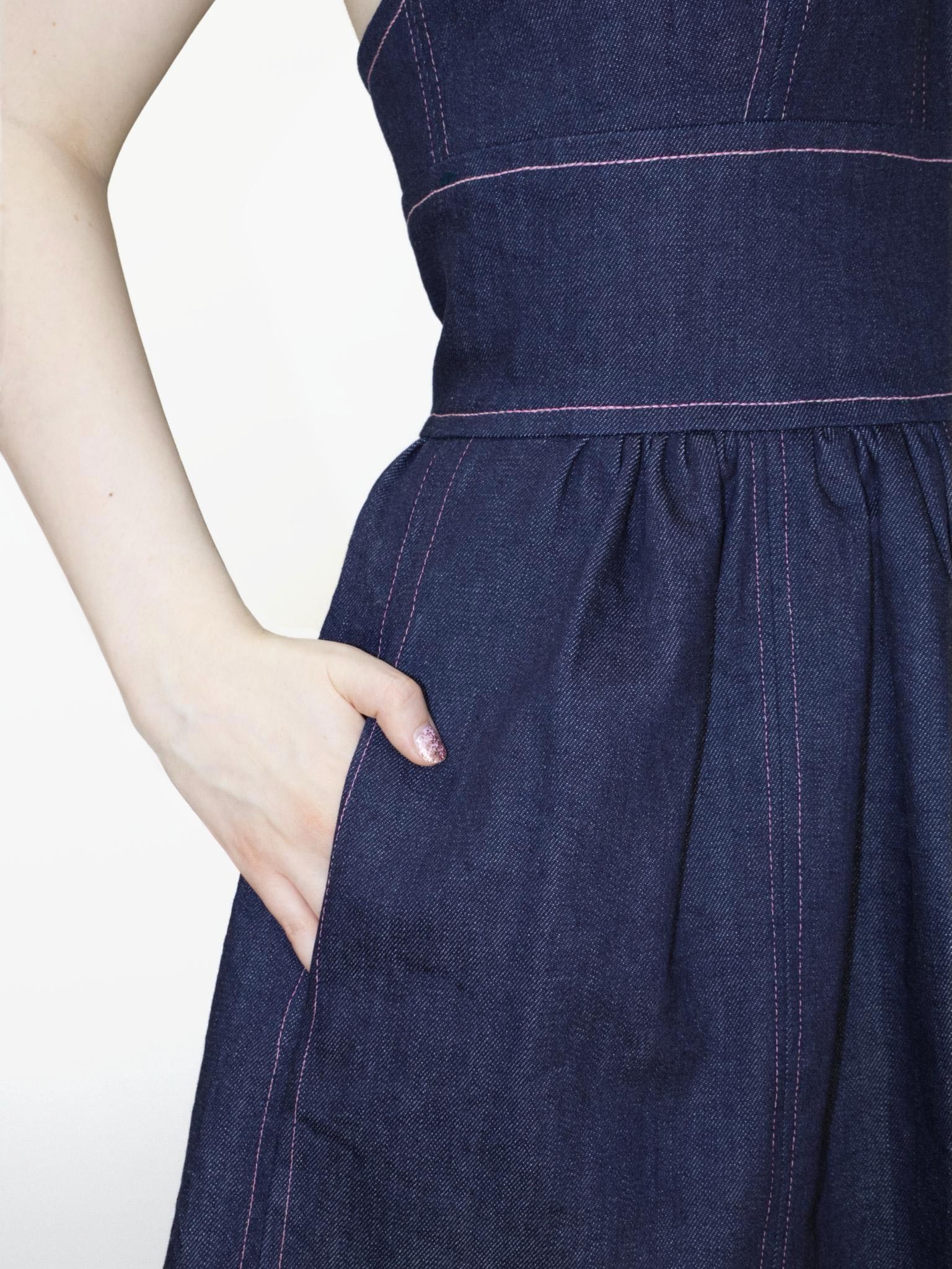 Detail view of a person wearing a denim mini dress with their hand in the skirts side seam pocket.