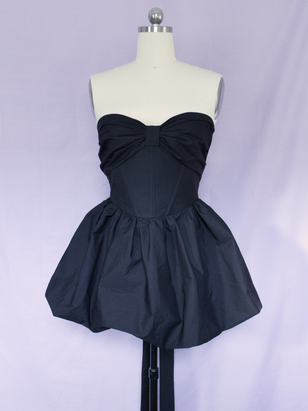 A black cotton strapless mini dress with voluminous bubble skirt and corset style bodice with a bow detail across the bust.