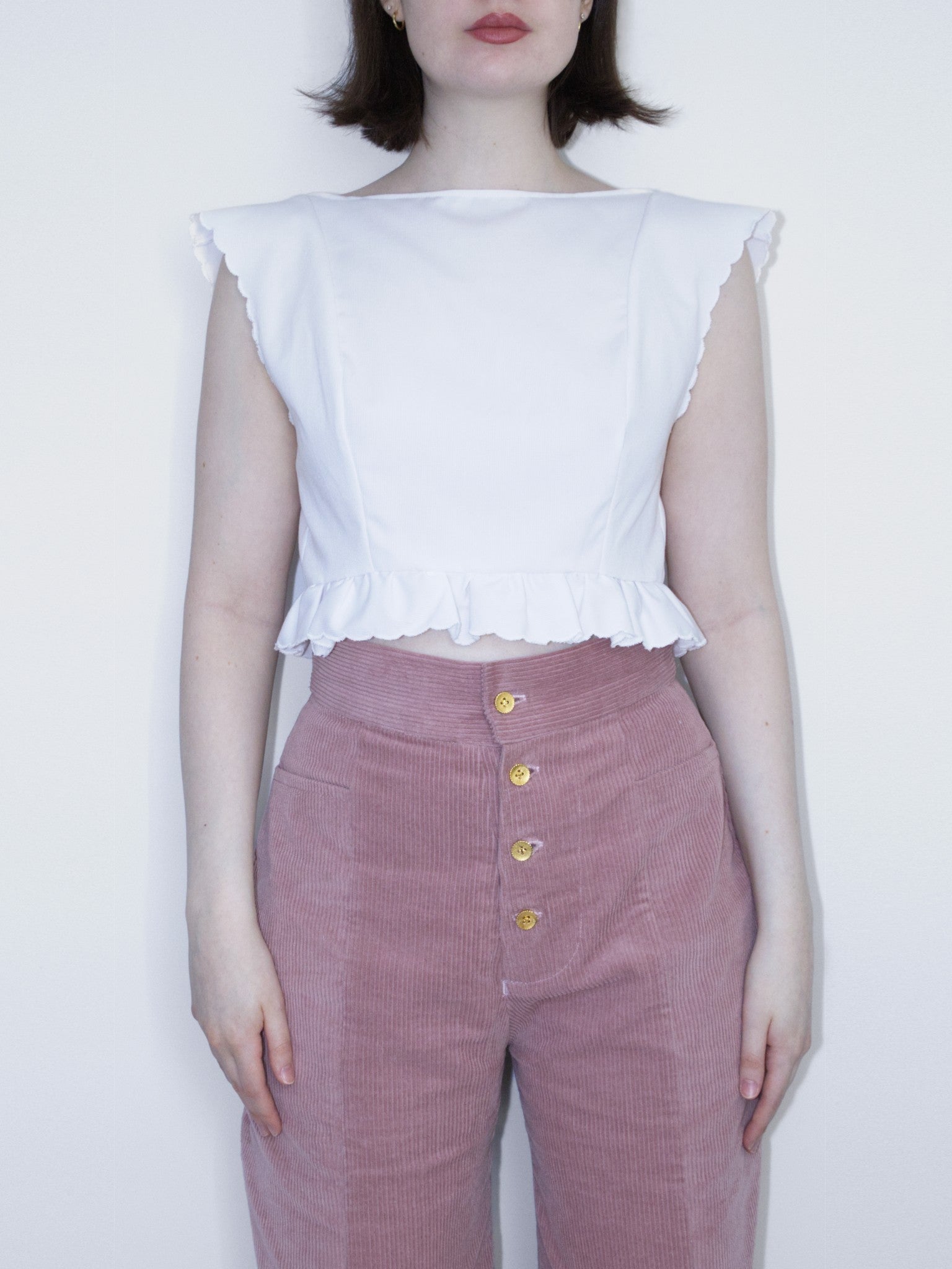 A white crop top with a boat neck, frill trim along the bottom, and a scalloped edge along the cap sleeves and bottom edge.