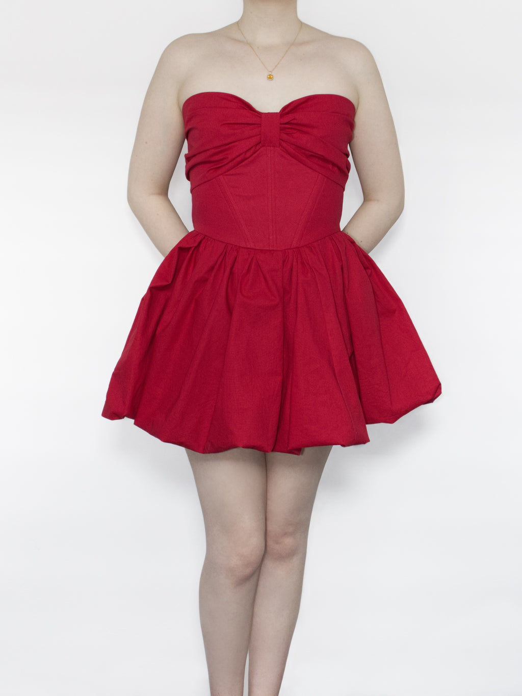 A red cotton strapless mini dress with sweetheart neckline and gathered bow design across the bust, corset style boned bodice and voluminous bubble skirt.