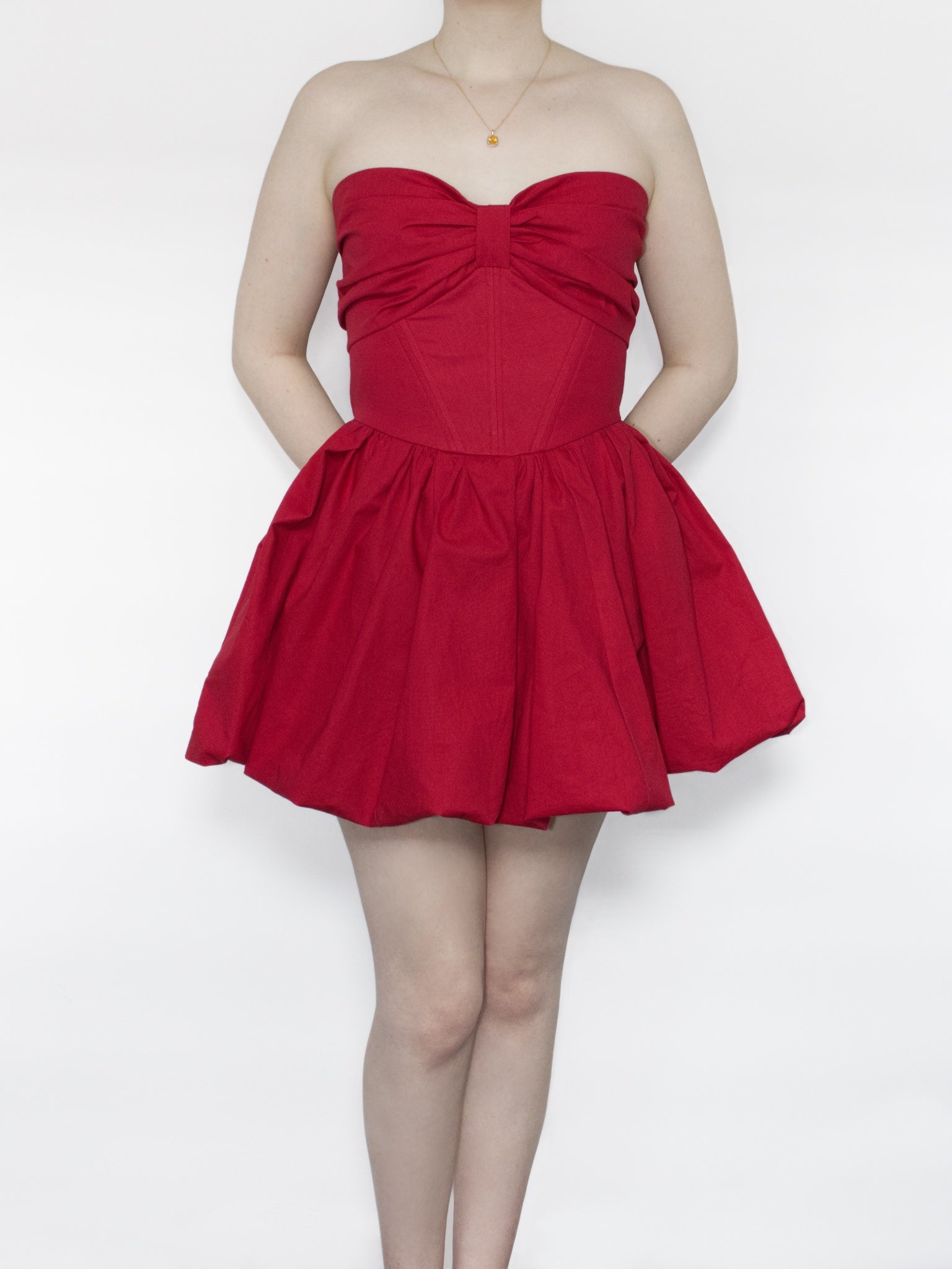 A red cotton strapless mini dress with sweetheart neckline and gathered bow design across the bust, corset style boned bodice and voluminous bubble skirt.
