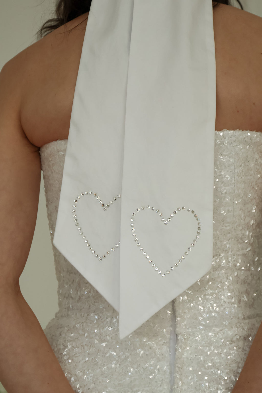 Close up of crystal hearts on the ends of the bow tails worn with a sequin bridal mini dress.