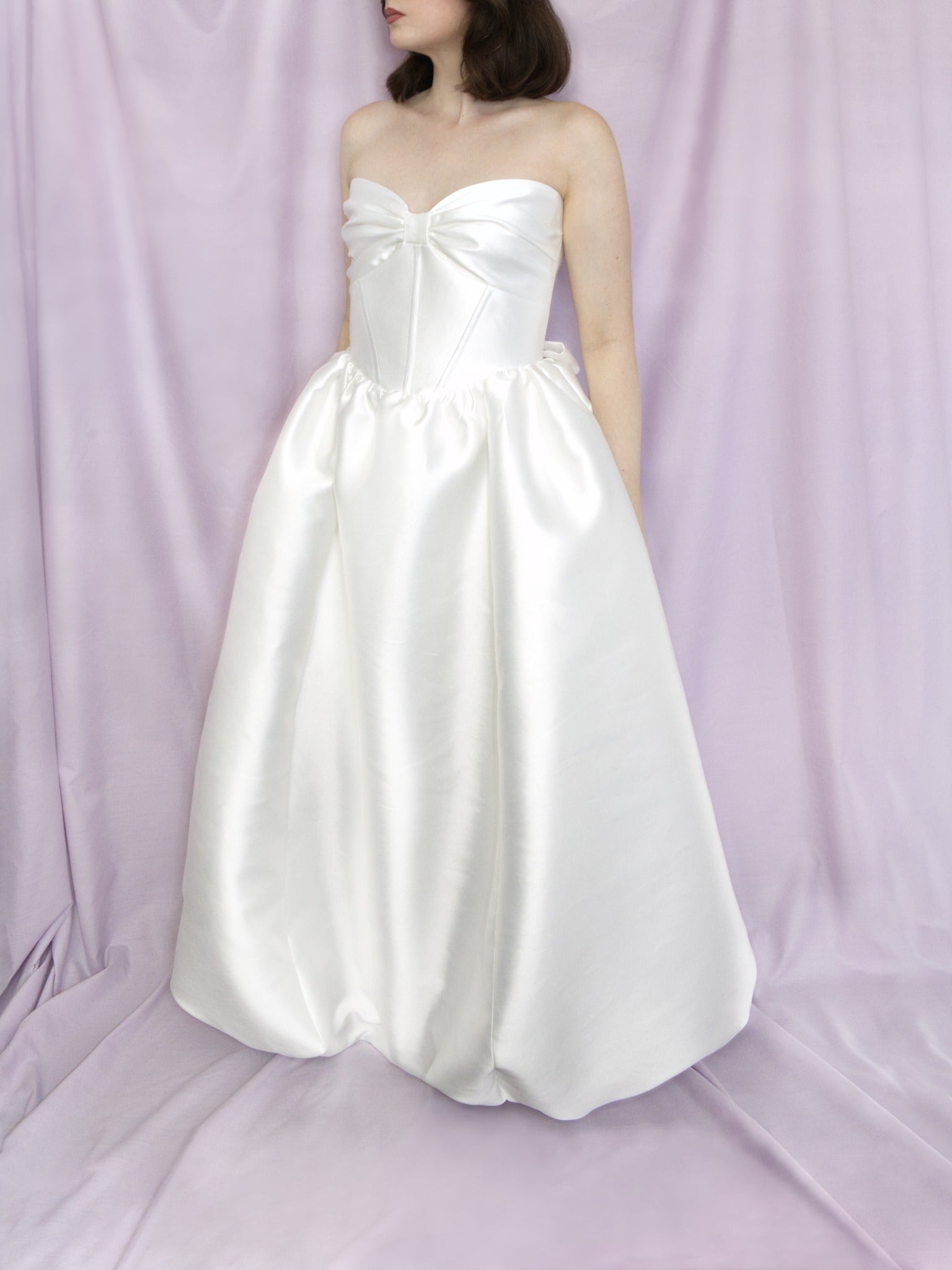 white lustrous strapless gown on a model against a purple background. 